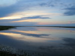 A flat, calm lake mirrors the fading sunlight in Montana